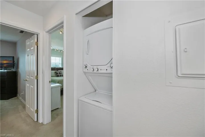 Clothes washing area featuring electric panel, stacked washer and clothes dryer, and light colored carpet