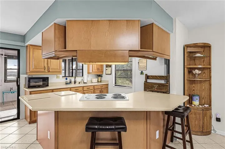 Kitchen with light tile floors, a breakfast bar area, light countertops, white electric stovetop, and brown cabinetry