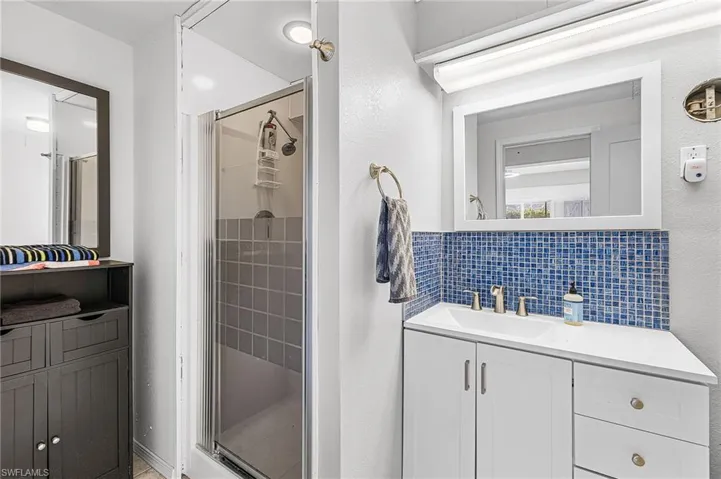 Full bathroom downstairs, with tasteful backsplash, vanity, a shower stall, and a textured wall