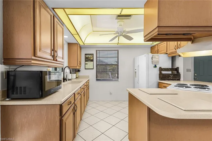 Kitchen with white appliances, a ceiling fan, light tile patterned floors, and brown cabinets