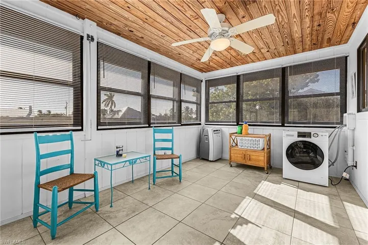 Laundry in glassed porch with wooden ceiling, tile patterned flooring, and a ceiling fan