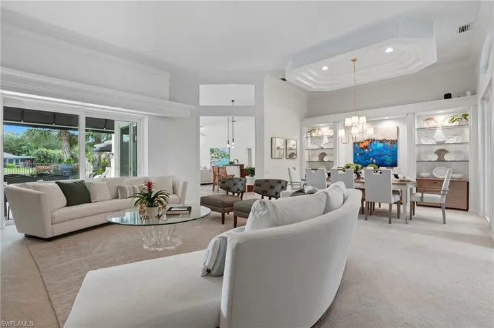 Living room featuring a chandelier, crown molding, light carpet, recessed lighting, and a tray ceiling