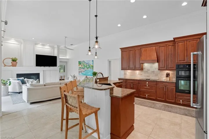 Kitchen featuring brown cabinetry, a kitchen bar, crown molding, an island with sink, and dark stone counters
