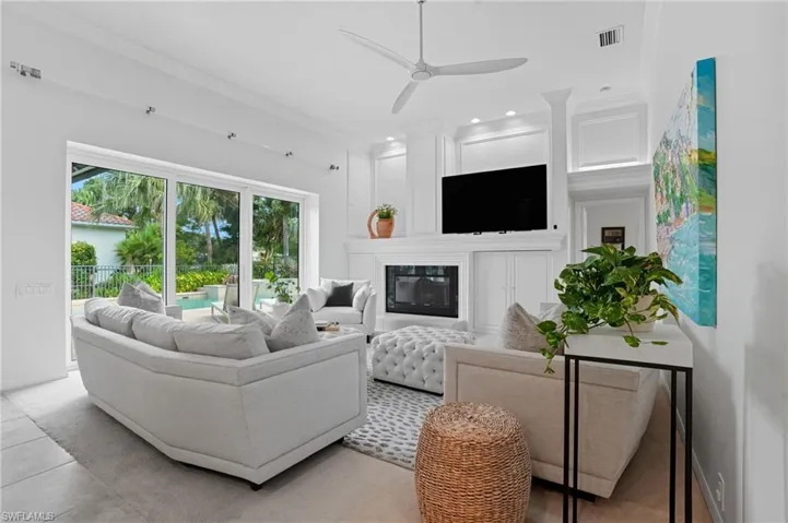 Tiled living area featuring a glass covered fireplace, ornamental molding, ceiling fan, and recessed lighting