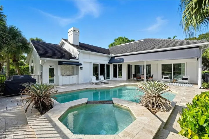 Rear view of house featuring a chimney, a patio area, a pool with connected hot tub, stucco siding, and a tiled roof