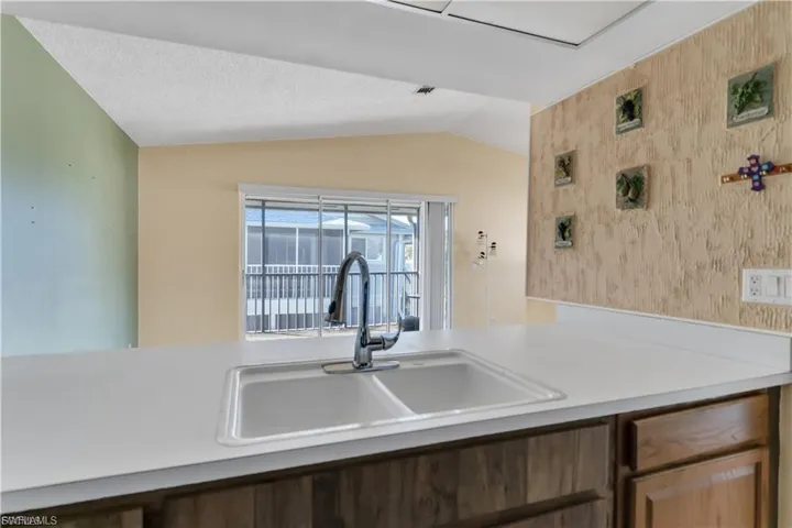 Kitchen with wallpapered walls, light countertops, lofted ceiling, and an accent wall