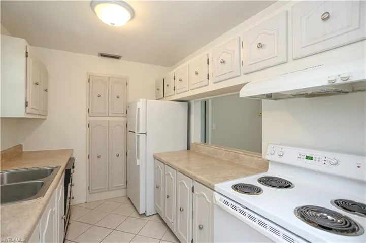 Kitchen featuring sink, range, white cabinets, light tile patterned floors, and white refrigerator