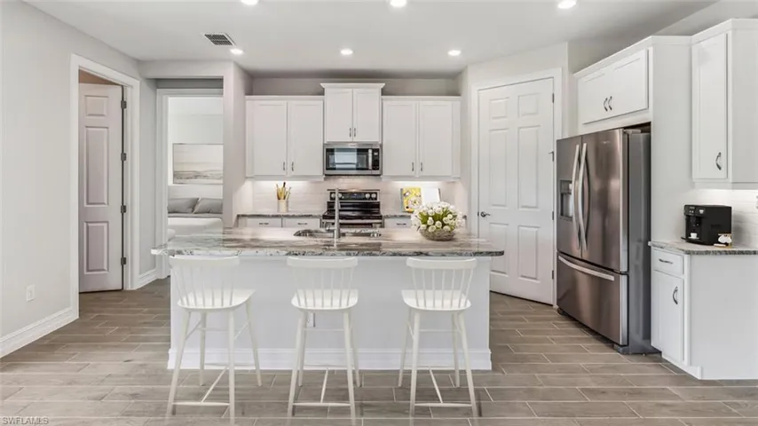 Contemporary kitchen featuring white cabinetry with brushed nickel hardware, stainless steel appliances including a gas range and refrigerator, granite countertops, a large center island with seating for three, recessed lighting, and wood-finish flooring throughout the open-concept space