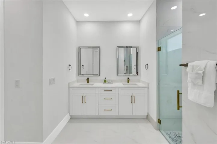Bathroom featuring a marble finish shower, light marble finish flooring, double vanity, and recessed lighting