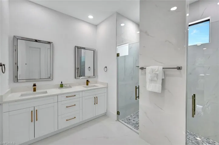 Full bathroom with a marble finish shower, double vanity, light marble finish flooring, and recessed lighting
