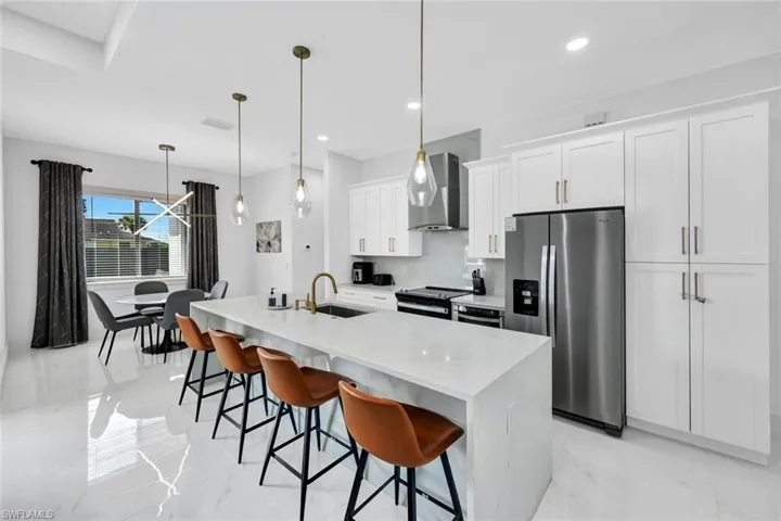 Kitchen featuring stainless steel fridge with ice dispenser, decorative light fixtures, white cabinets, light marble finish flooring, and electric stove