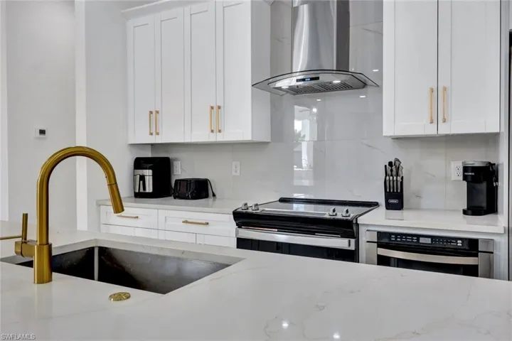 Kitchen with extractor fan, white cabinets, electric stove, and light stone counters