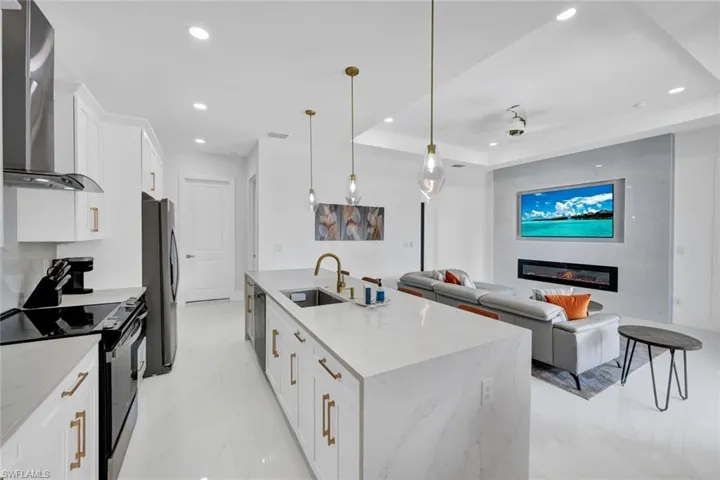Kitchen featuring range with electric cooktop, white cabinets, wall chimney exhaust hood, hanging light fixtures, and light marble finish floors