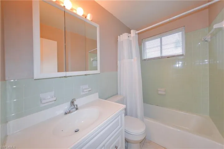 Full bathroom featuring vanity, tasteful backsplash, shower / bath combination with curtain, tile walls, and toilet