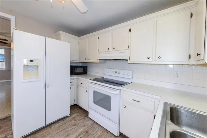 Kitchen featuring white appliances, white cabinets, decorative backsplash, sink, and light hardwood / wood-style flooring