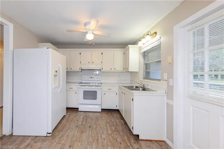 Kitchen with white appliances, white cabinetry, sink, light wood-type flooring, and backsplash