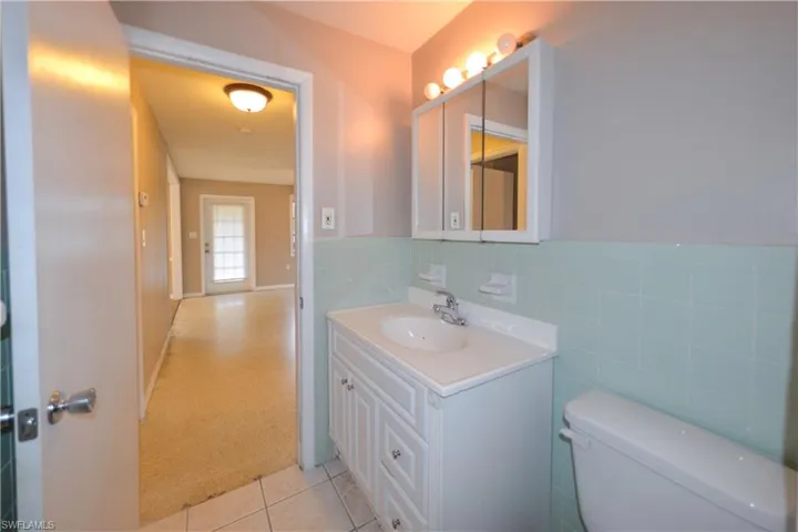 Bathroom with tile walls, toilet, vanity, and tile patterned flooring