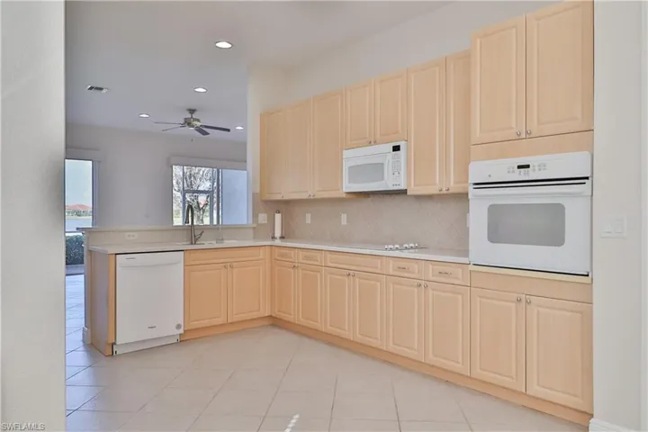 Kitchen with kitchen peninsula, backsplash, light tile patterned floors, white appliances, and ceiling fan