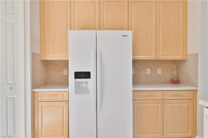 Kitchen featuring decorative backsplash, white refrigerator with ice dispenser, and light brown cabinets