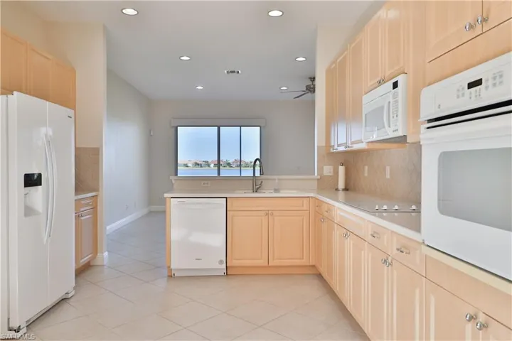 Kitchen with white appliances, tasteful backsplash, light brown cabinetry, sink, and light tile patterned floors