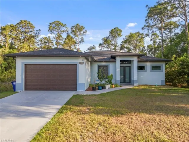 View of front of home with stucco siding, french doors, a front yard, concrete driveway, and an attached garage
