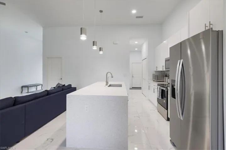 Kitchen featuring a sink, marble finish floor, white cabinets, appliances with stainless steel finishes, and open floor plan