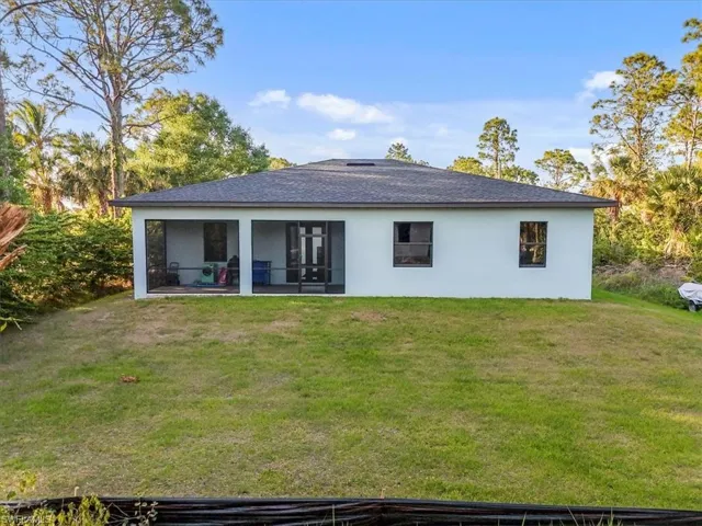 Back of property featuring stucco siding, a shingled roof, a sunroom, and a lawn
