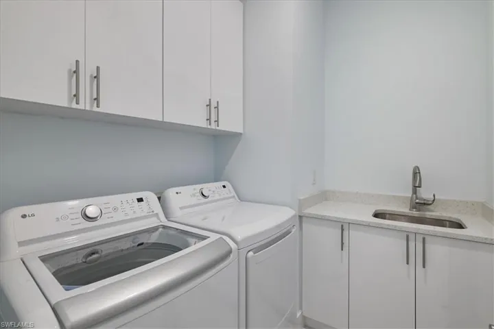 Clothes washing area featuring separate washer and dryer, a sink, and cabinet space