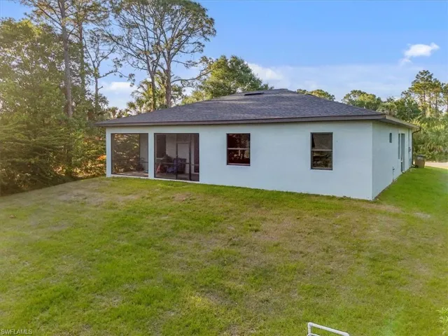 Rear view of property featuring roof with shingles, stucco siding, and a lawn