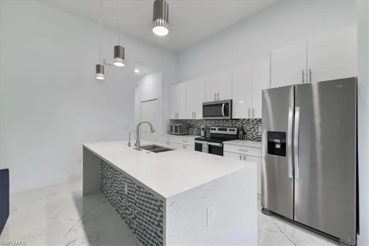 Kitchen featuring an island with sink, stainless steel appliances, marble finish floor, backsplash, and a sink