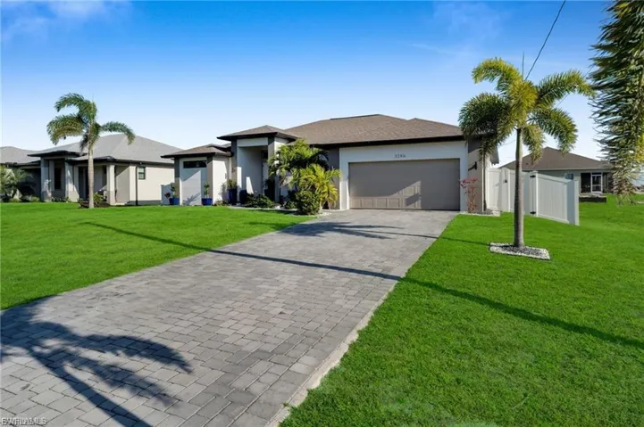 View of front of home featuring decorative driveway, stucco siding, a garage, and a gate