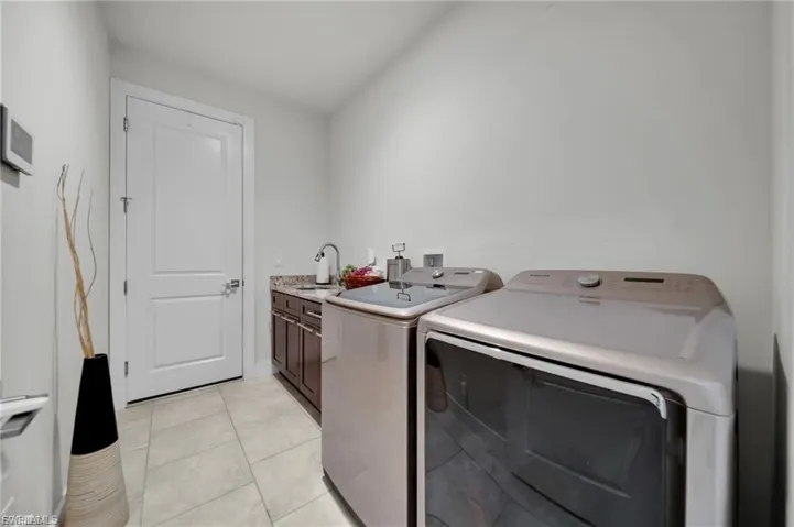 Laundry area featuring light tile patterned floors, washing machine and clothes dryer, and cabinet space