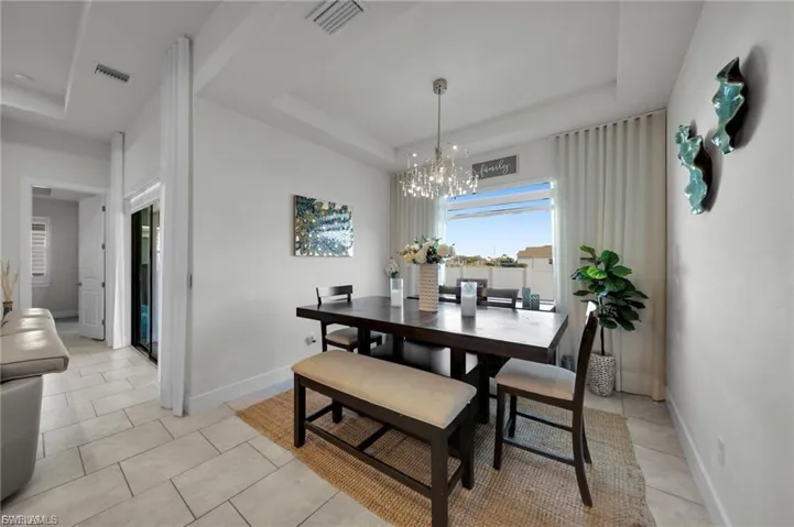 Dining room featuring a tray ceiling, a chandelier, and light tile patterned flooring