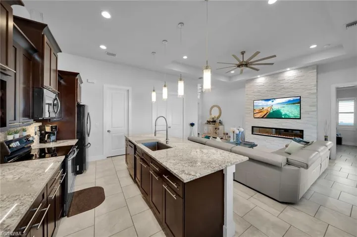 Kitchen with black appliances, dark wood finish cabinetry, light stone counters, open floor plan, and a raised ceiling
