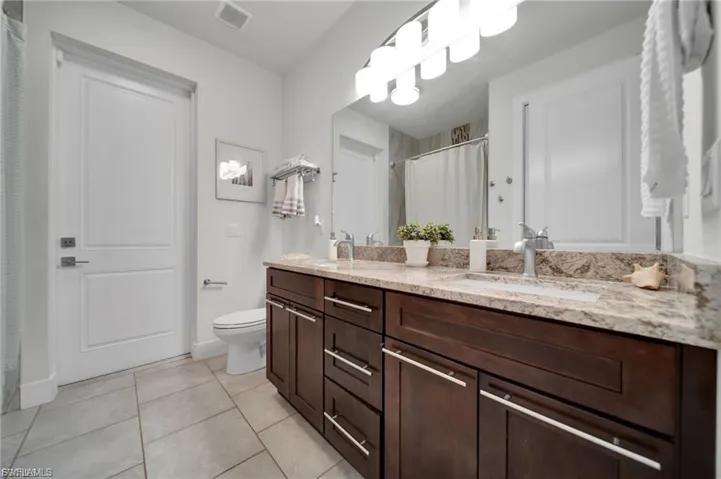 Bathroom featuring a shower with shower curtain, double vanity, and light tile patterned floors