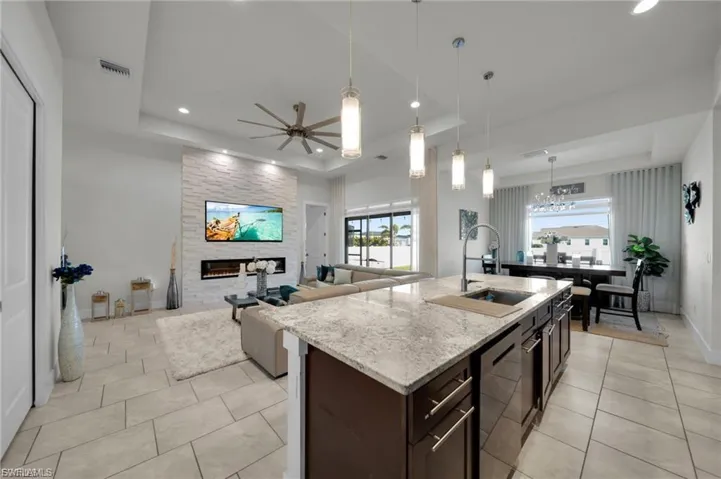 Kitchen with dark wood finish cabinets, a fireplace, ceiling fan, decorative light fixtures, and light stone countertops