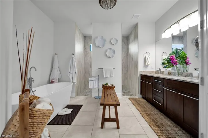 Bathroom with a walk in shower, a freestanding tub, vanity, and light tile patterned flooring