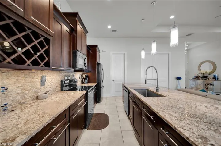 Kitchen featuring dark wood finish cabinets, black appliances, light stone counters, and decorative light fixtures