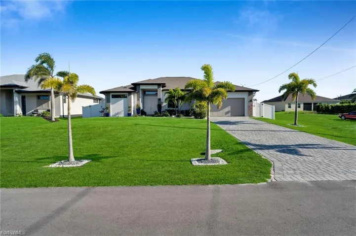 View of front of house featuring a front lawn, decorative driveway, an attached garage, and stucco siding