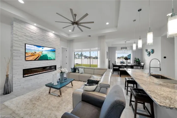 Living area with a stone fireplace, ceiling fan, recessed lighting, a raised ceiling, and light tile patterned floors