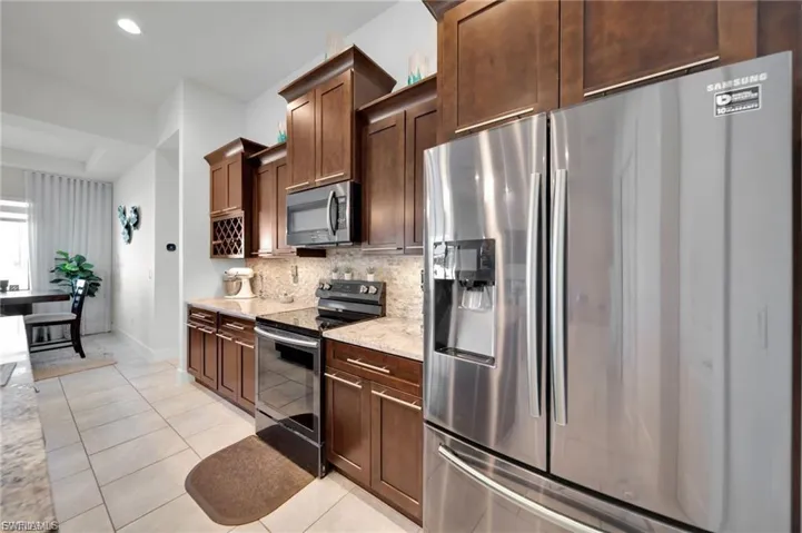 Kitchen with stainless steel appliances, light tile patterned flooring, light stone countertops, dark wood finish cabinetry, and recessed lighting