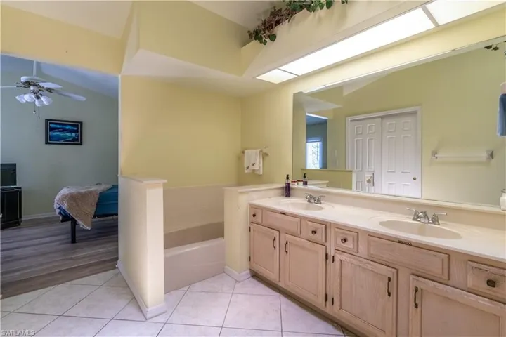 Bathroom with tile patterned floors, a bath, lofted ceiling, ceiling fan, and vanity