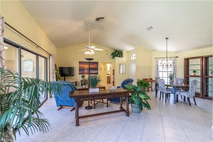 Living room with lofted ceiling, ceiling fan with notable chandelier, and light tile patterned floors