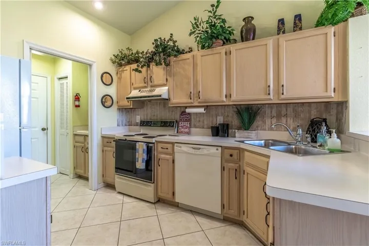 Kitchen with white appliances, light brown cabinetry, light tile patterned floors, sink, and decorative backsplash