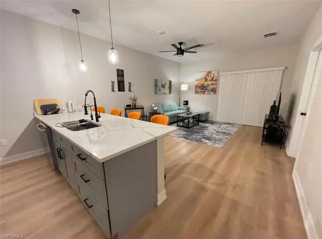 Kitchen featuring a peninsula, pendant lighting, light stone countertops, light wood-type flooring, and a breakfast bar area