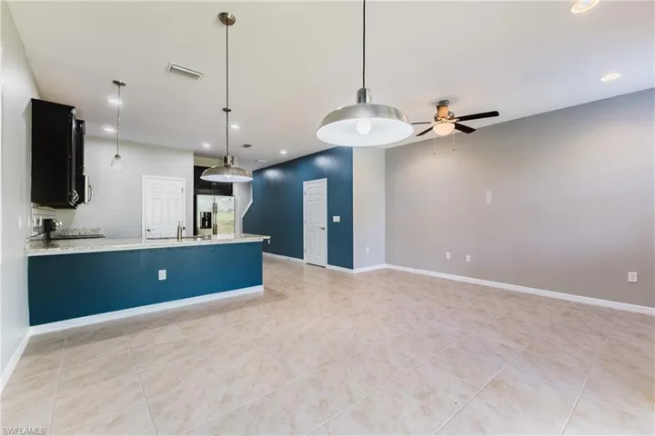Kitchen featuring pendant lighting, light stone counters, stainless steel refrigerator with ice dispenser, and a ceiling fan