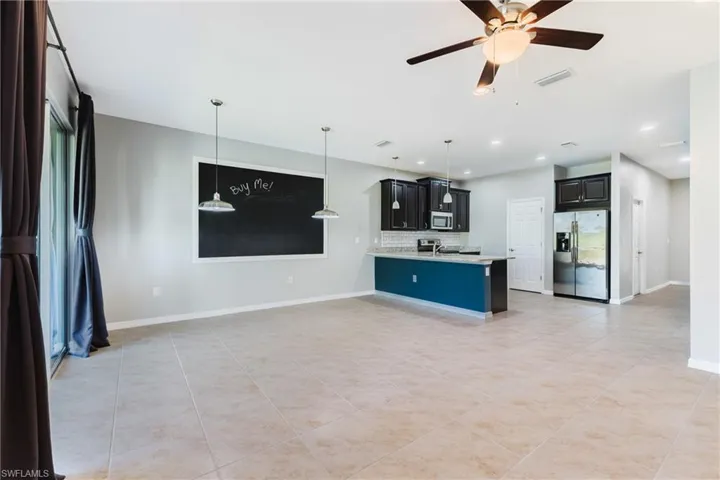 Kitchen with dark cabinetry, stainless steel appliances, open floor plan, a ceiling fan, and pendant lighting