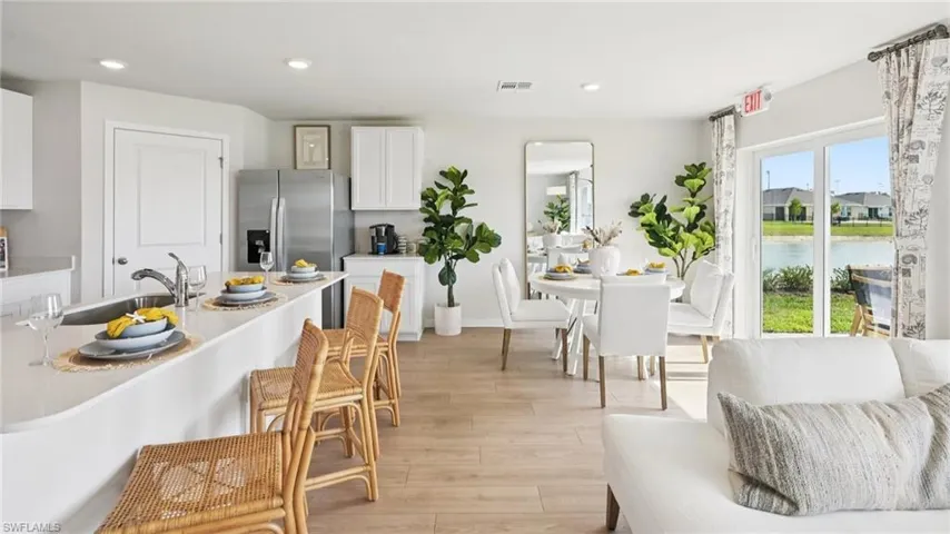 Model Home. Open concept living area featuring light wood-style flooring, a kitchen island with seating, and a dining area with views of the outdoor landscape