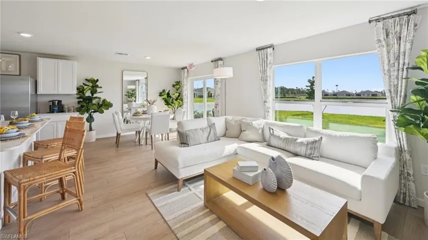 Model Home. Open concept living area featuring light-toned flooring, large windows with views of a body of water, and recessed lighting