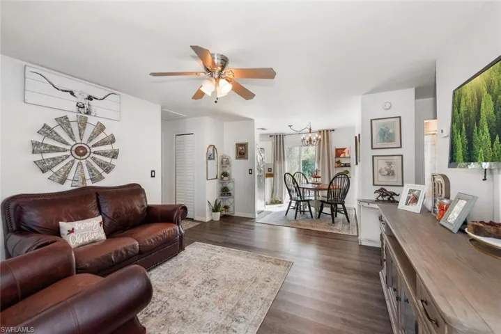 Living area with dark wood-type flooring, a ceiling fan, and a chandelier